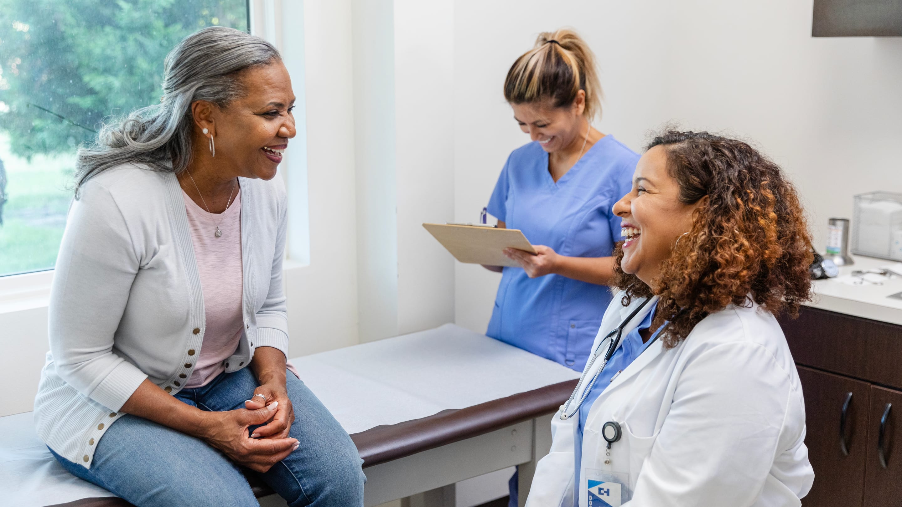 The senior adult woman shares a lighthearted moment with the mature adult female doctor and the mid adult female nurse.