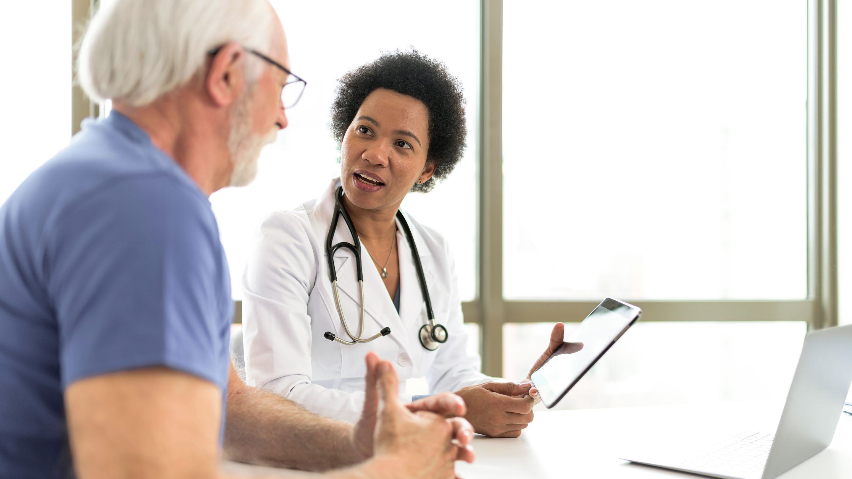 Image of a serious retired man consulting with younger female physician at the checkup meeting in the hospital.