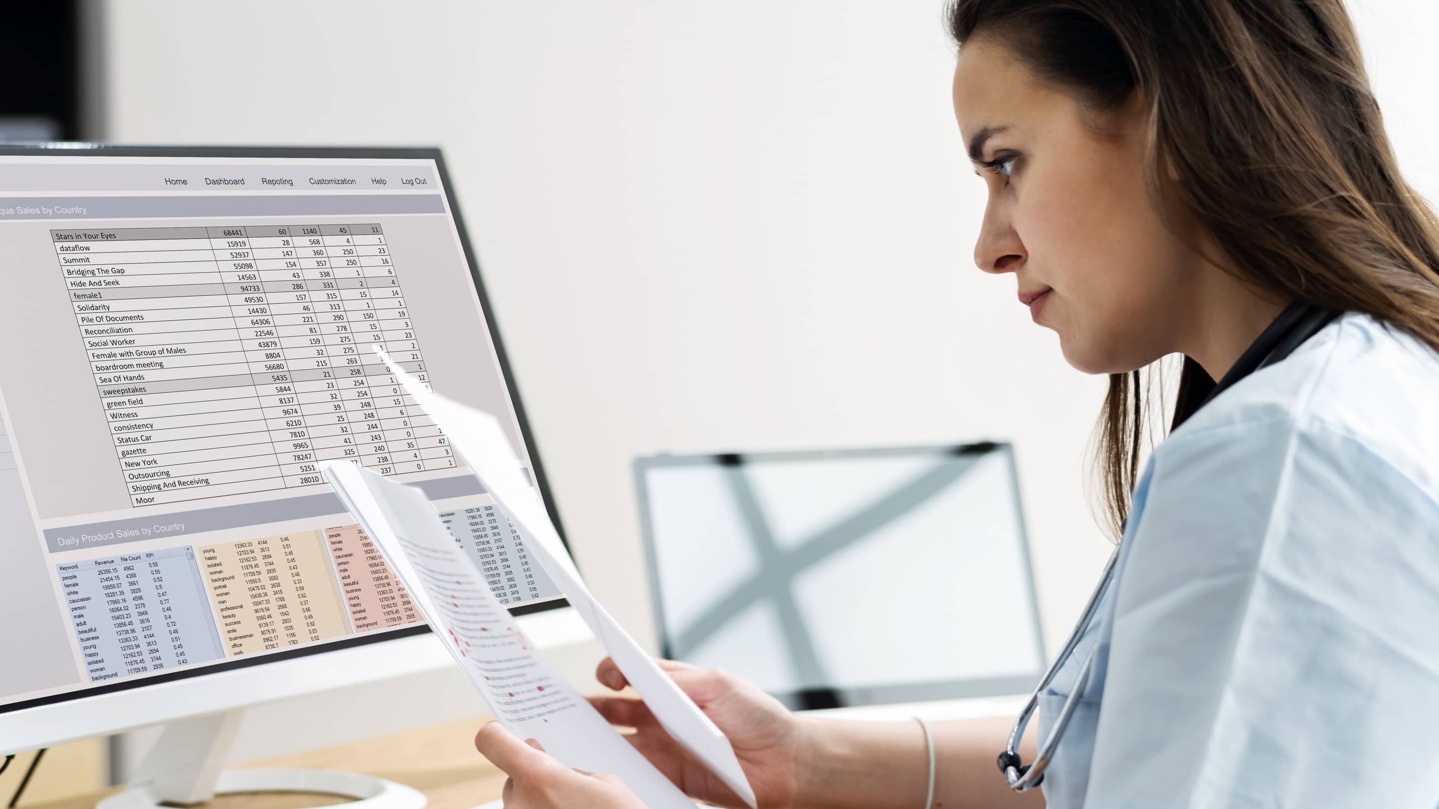 Smiling woman sitting in front of a computer holding papers in one hand.