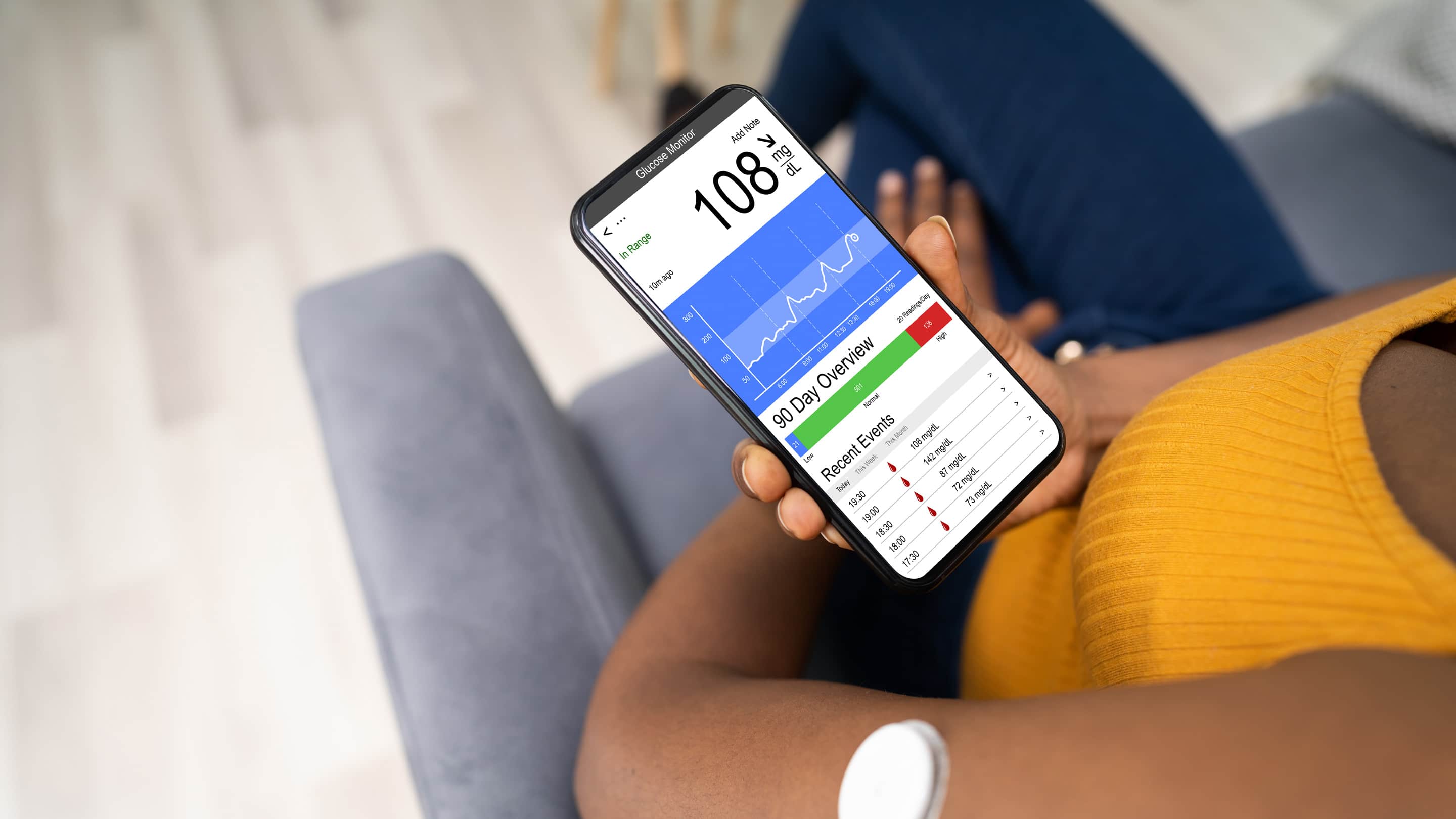 View of a CGM device on a patient’s arm while they hold a mobile phone with readings of the device.