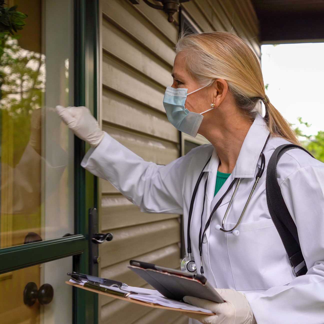 Rural medicine—Physician arriving for home visit in rural area, knocking and smiling at door.