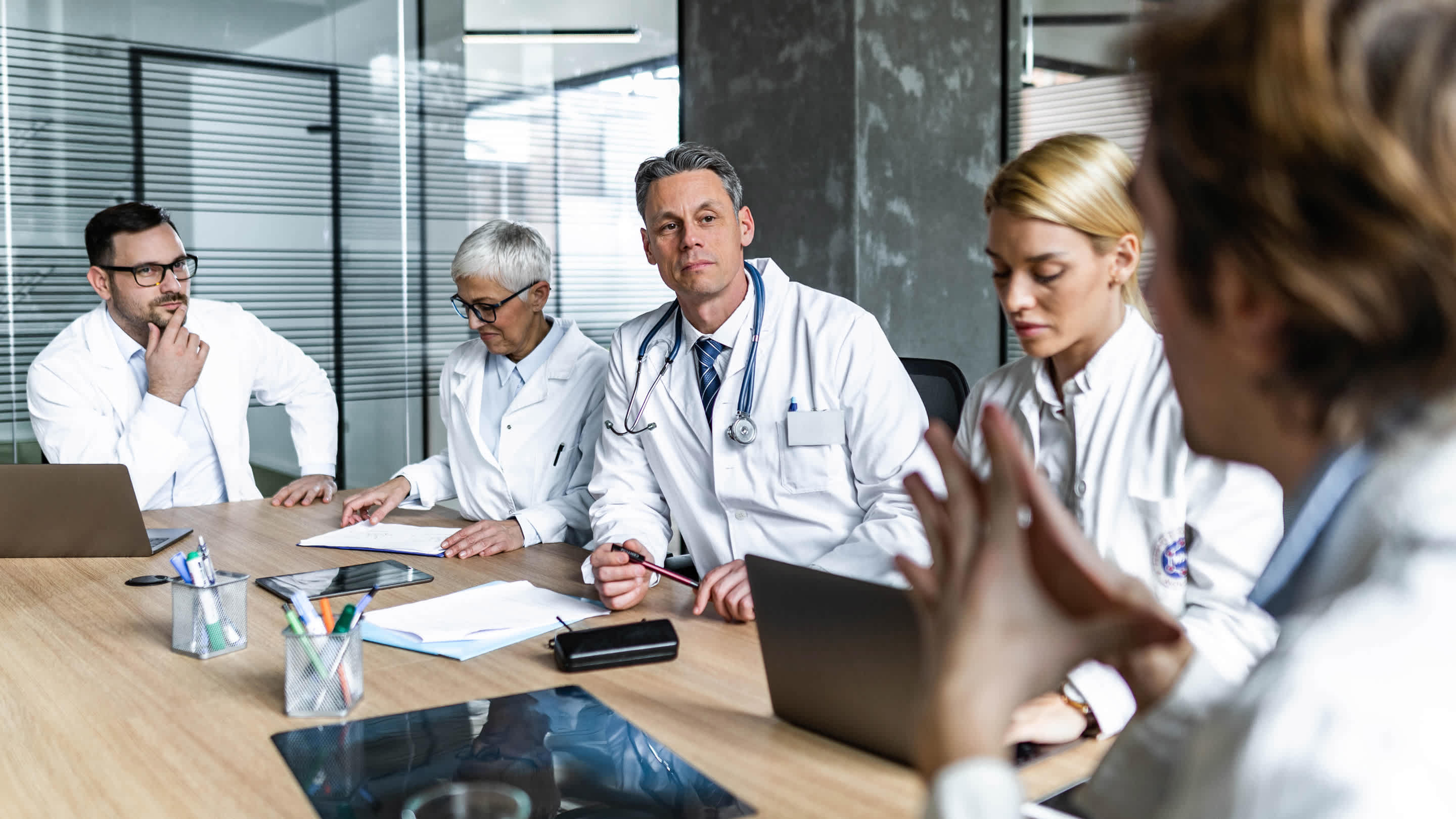 Multiple family physicians in a room/practice listening to another doctor talk about something.