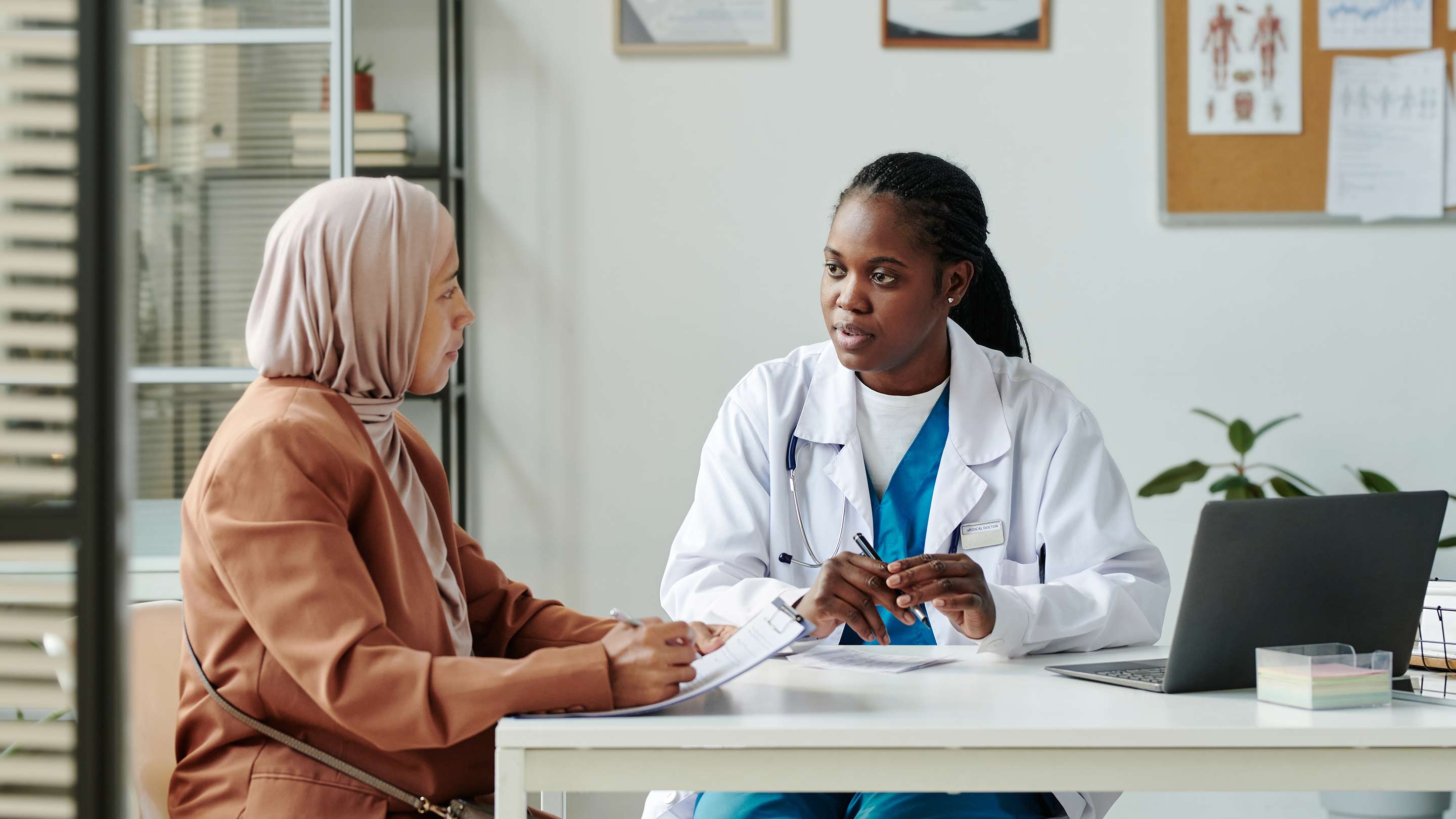 Young African American female clinician in lab coat talking to patient.