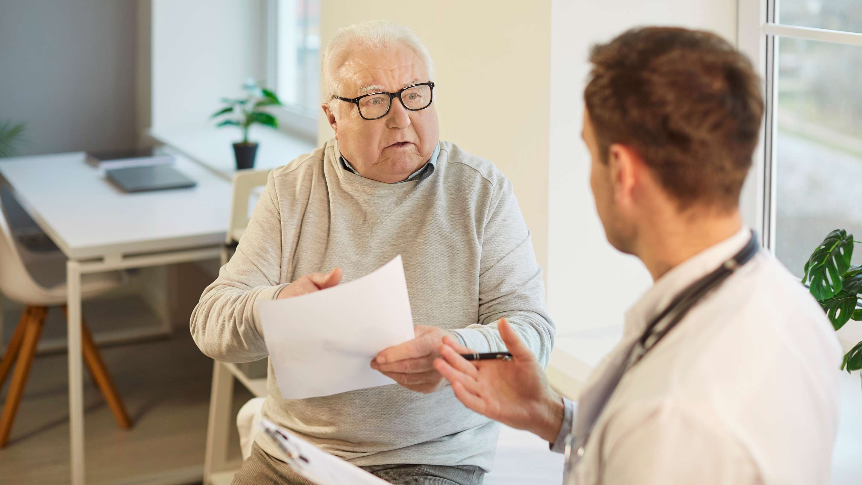 Senior retired gray-haired man talking to a male doctor in his office.