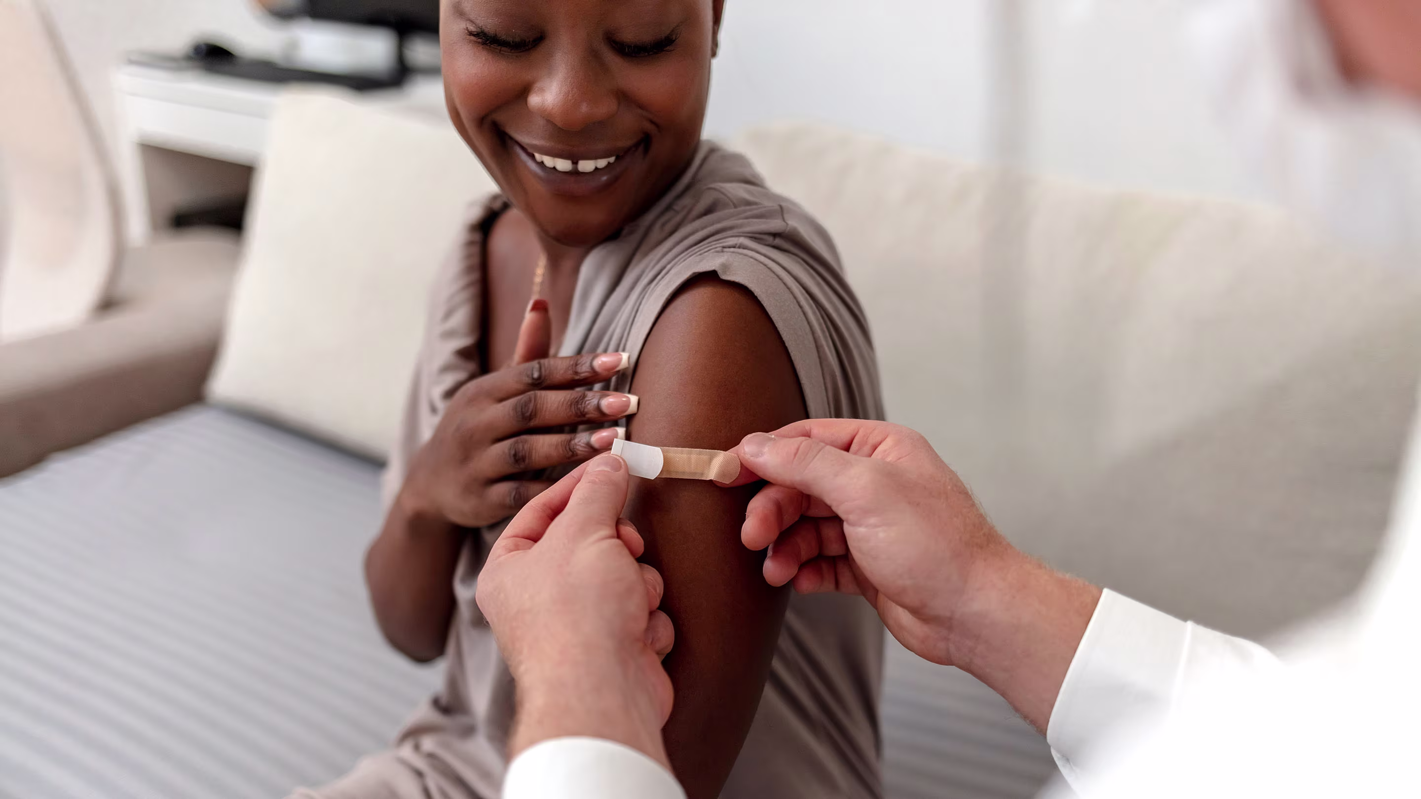 Smiling patient gets bandaid from doctor after a vaccination or blood draw.