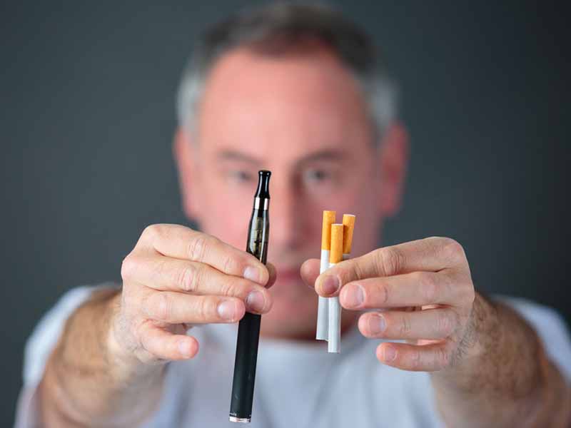 Man holding combustible cigarettes and e-cigarette