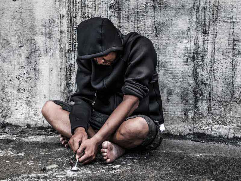 youth squatting on ground with spoon for using opioids