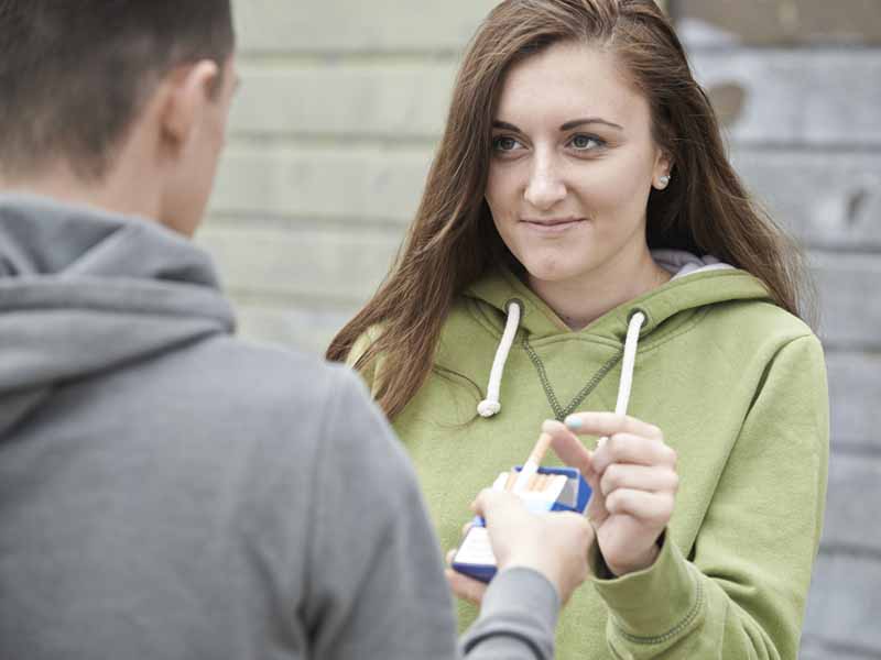 teen girl accepting cigarette from teen boy