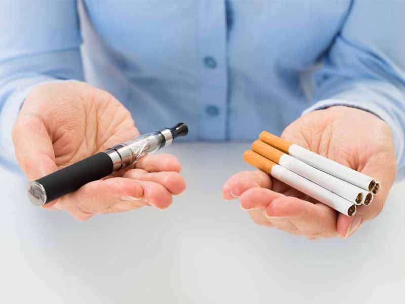 man holding e-cigarette in one hand and traditional cigarettes in the other