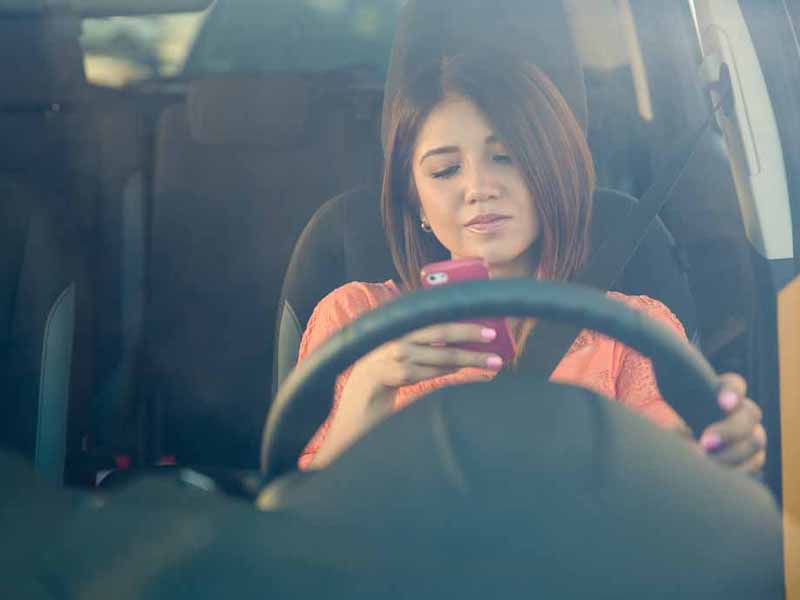 teen girl looking at phone while driving