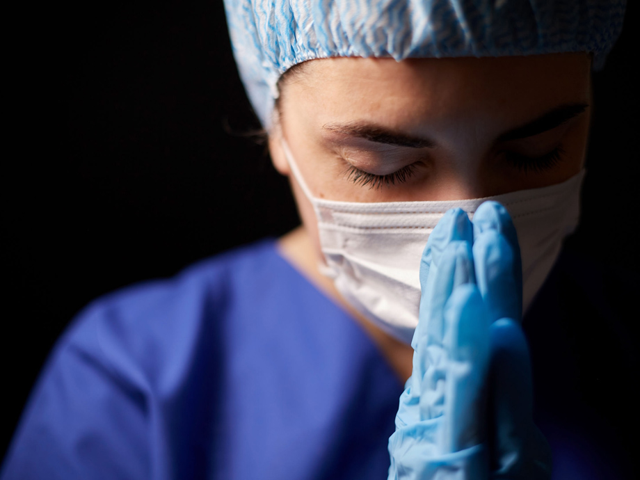 health, medicine and pandemic concept - sad young female doctor or nurse wearing face protective mask for protection from virus disease praying over black background