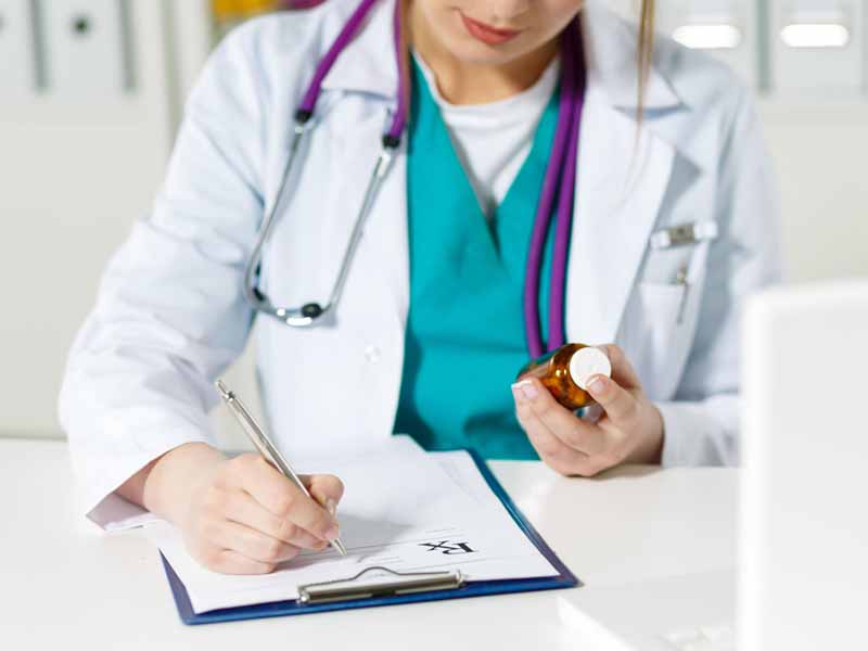 41502918 - beautiful young female doctor sitting in front of working table holding jar of tablets and writing prescription on special form. medical and pharmacist concept.