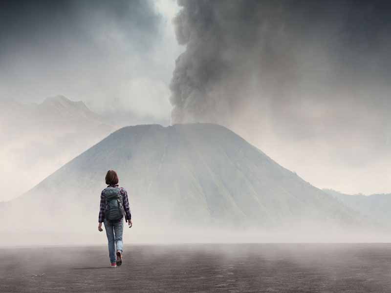 20933719 - hiker with backpack crossing valley with ash towards active volcano