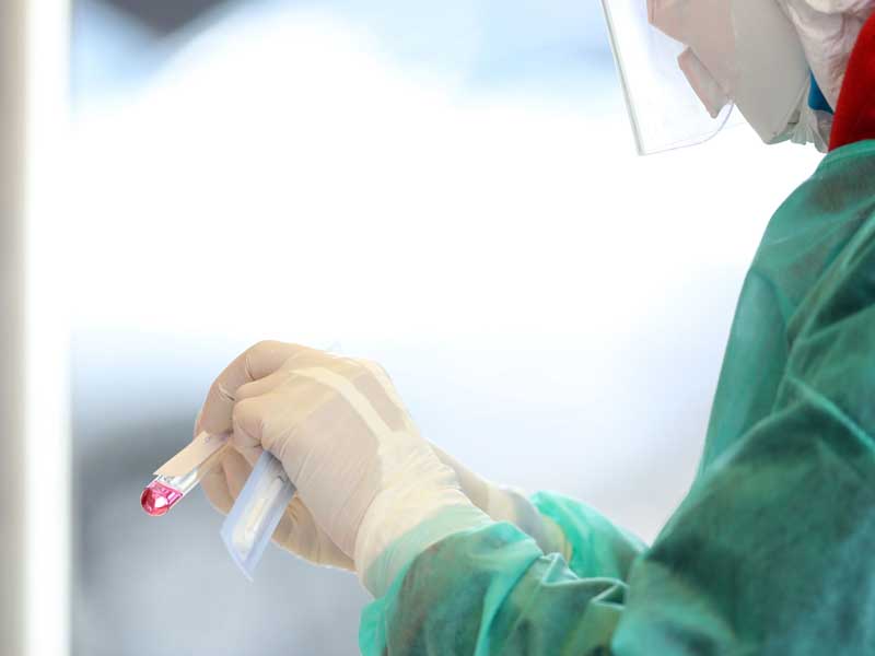 Medical staff member with mask and protective equipment holds Coronavirus nasal swabs test tubes at drive-through testing point in an effort to curb the spread of COVID-19 (novel coronavirus)