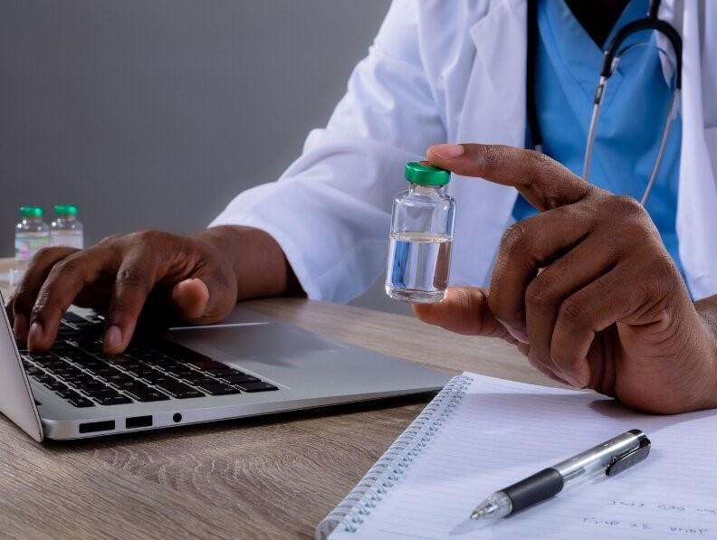Male physician at a laptop holding a vaccine vial