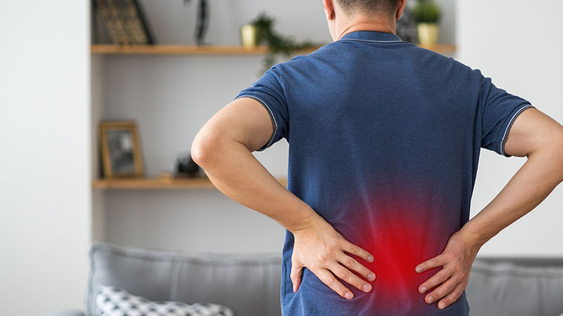a male places his hands on his lower back in pain