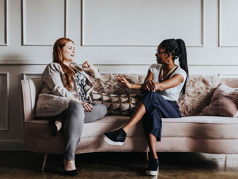 Two females talk to each other while sitting on a couch