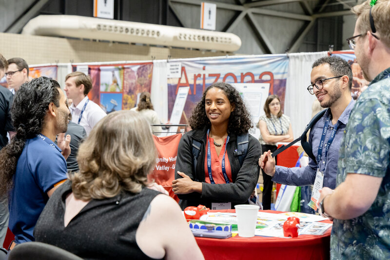 Two woman and three men talking together at a booth on the expo hall floor