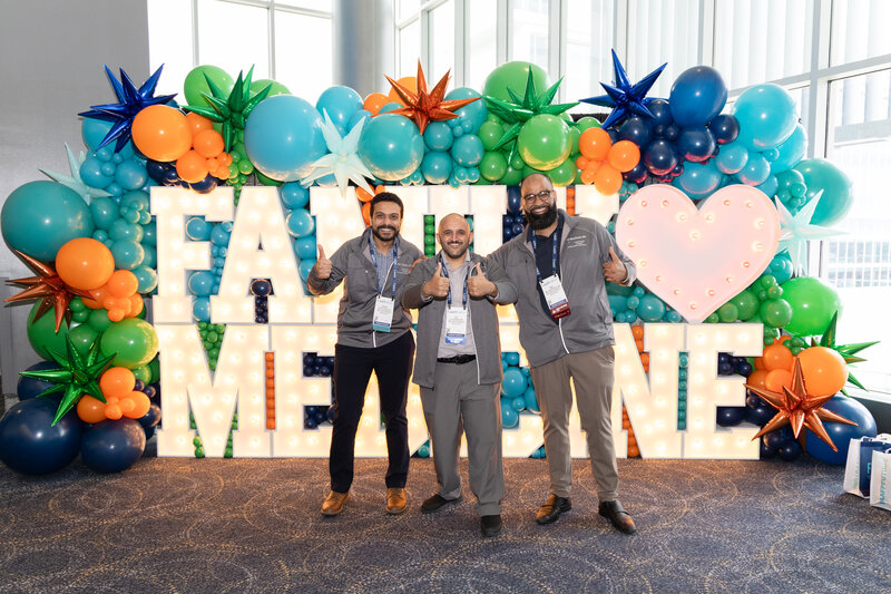 Three men standing in front of Family Medicine letters with balloons giving thumbs up