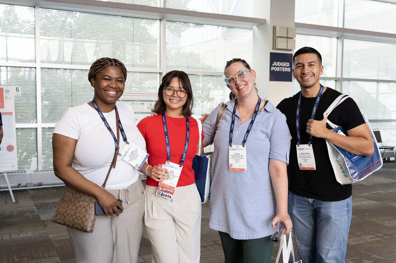 three woman and one man standing in a row smiling in a convention center hallway