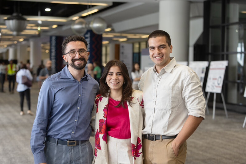 Two men and one woman attendees smiling standing in the convention center hallway