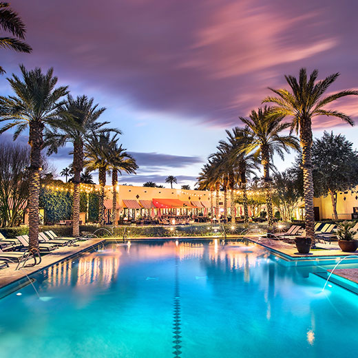 Outside pool view at dusk with lounge chairs and palm trees