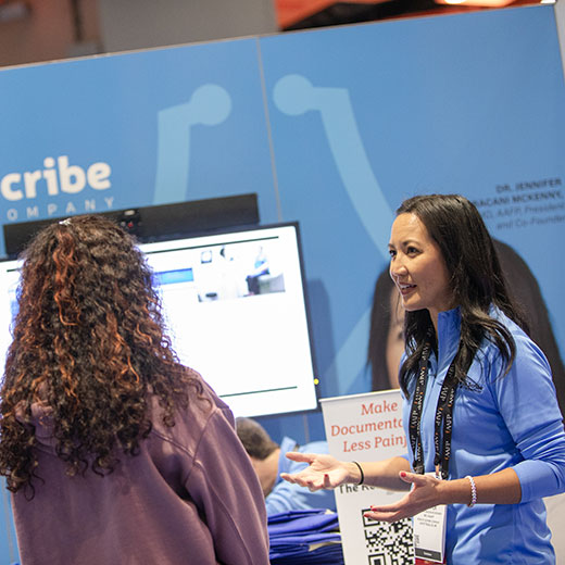 An exhibitor talks to a doctor attendee about electronic scribe services at FMX 2023.