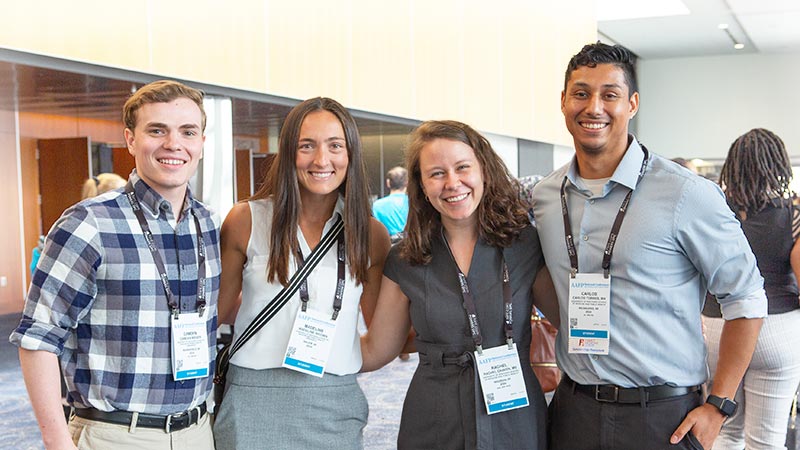 Four young professionals standing in a row smiling at a conference