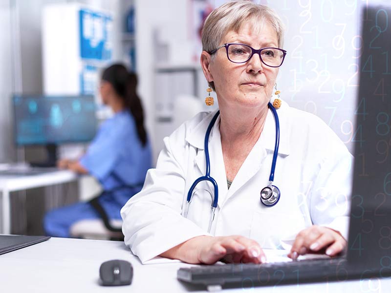 Older female physician entering patient visit documentation on desktop computer