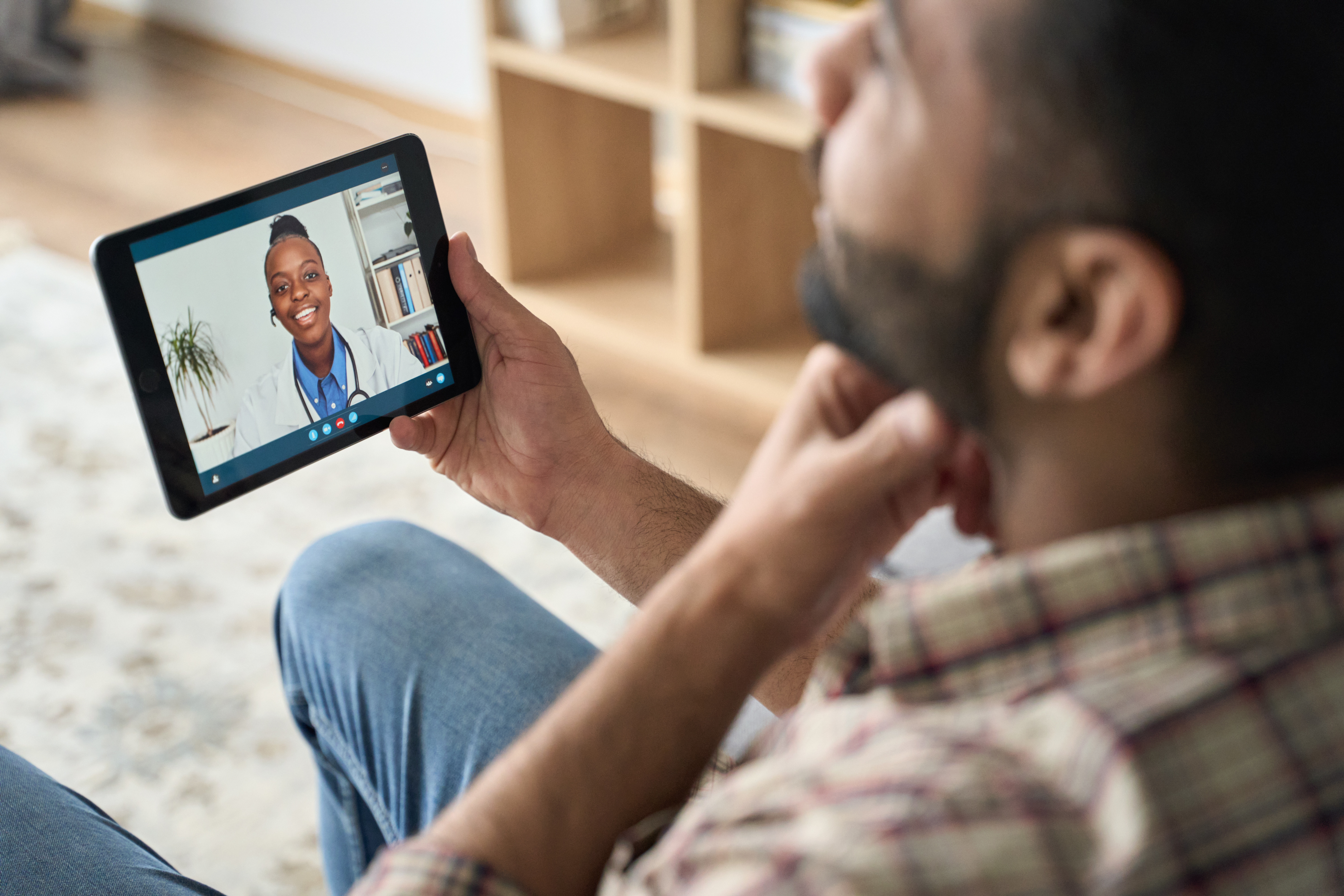 Young indian latin bearded businessman having videocall meeting at home with black female doctor therapist using tablet computer pointing to throat. Online virtual telemedicine health care concept.