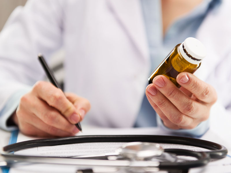 physician writing notes and looking at pill bottle