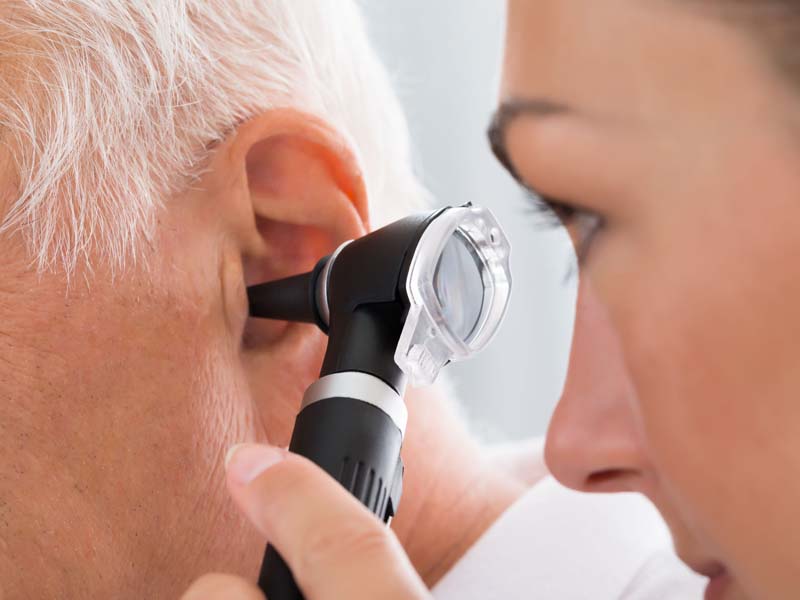 physician examining older patient's ear