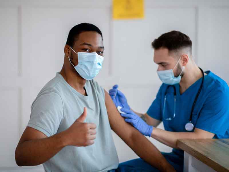 Man in mask gesturing thumb up during coronavirus vaccination
