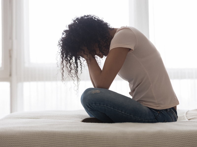 Despondent woman huddled on bed holding head in her hands