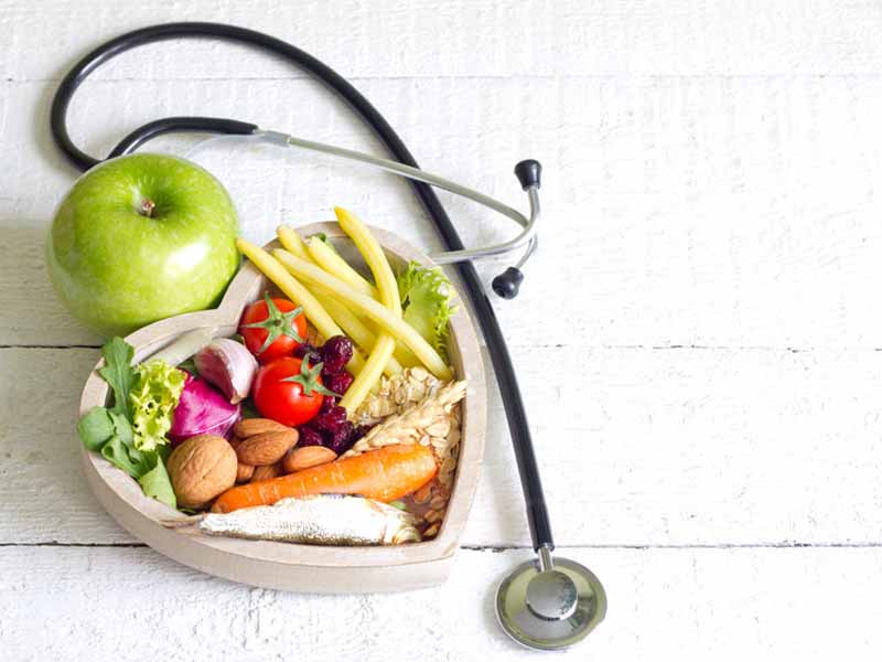 Fruits, vegetables, grains and nuts on a heart-shaped plate next to a stethoscope