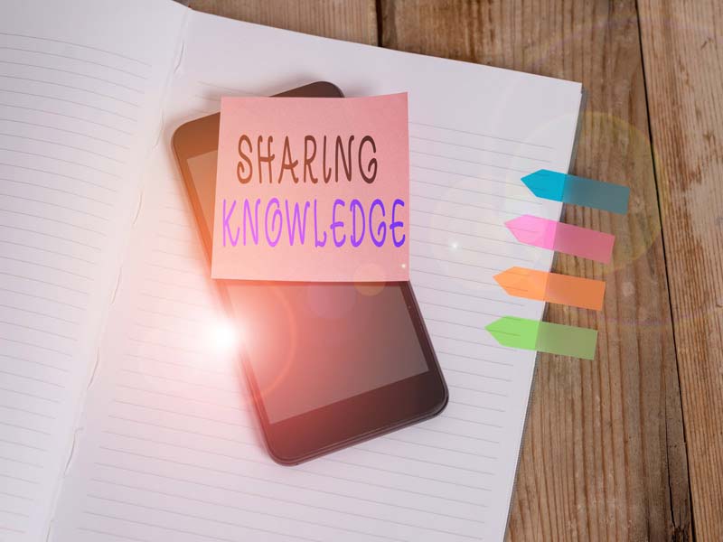 Note reading "sharing knowledge" stuck on a smartphone sitting on a notebook