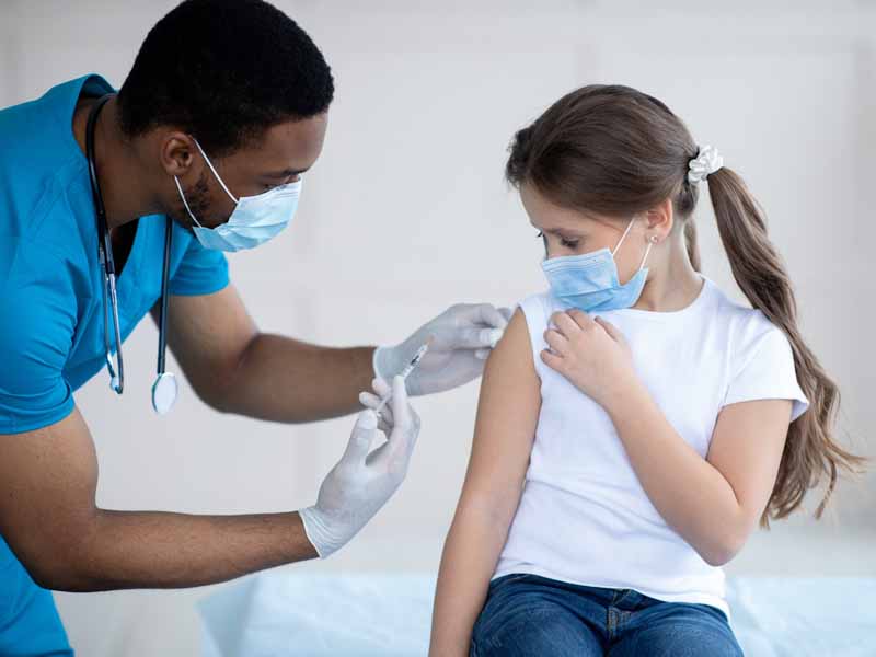 Masked physician administering vaccine to masked girl