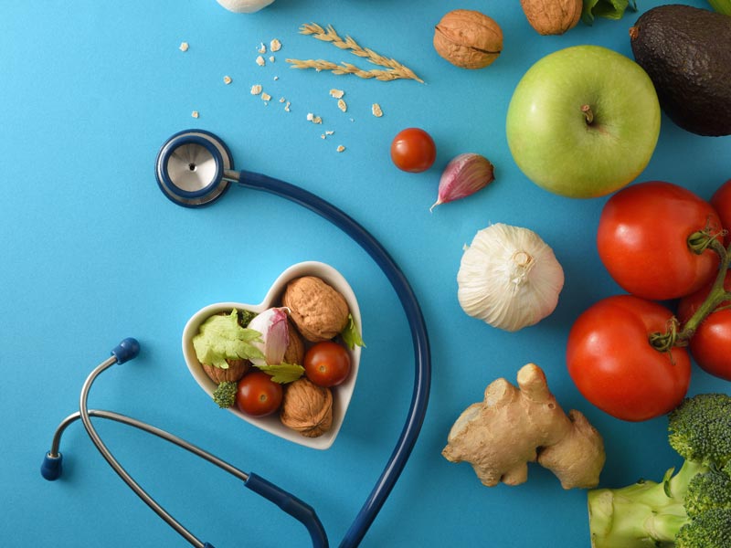 Stethoscope on blue background with fruits, vegetables, nuts, grain, herbs and spices