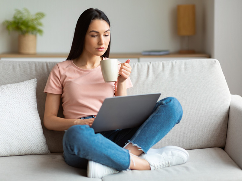 young woman sitting on couch looking at laptop