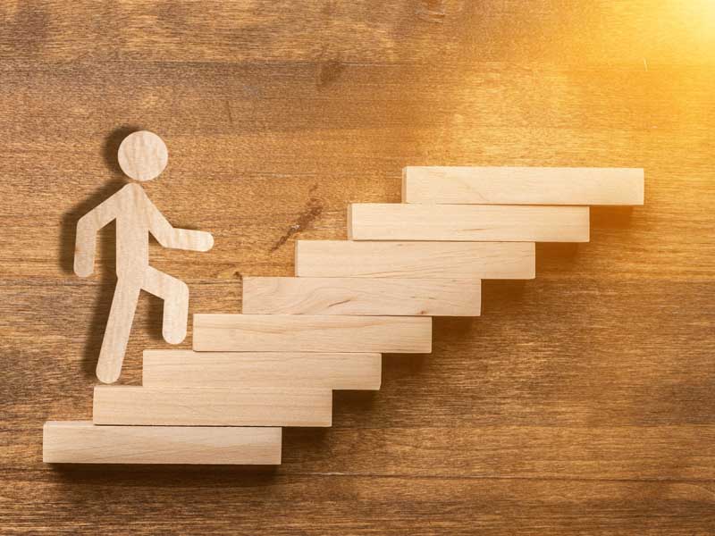 Success concept with wooden businessman climbing wooden block stairs