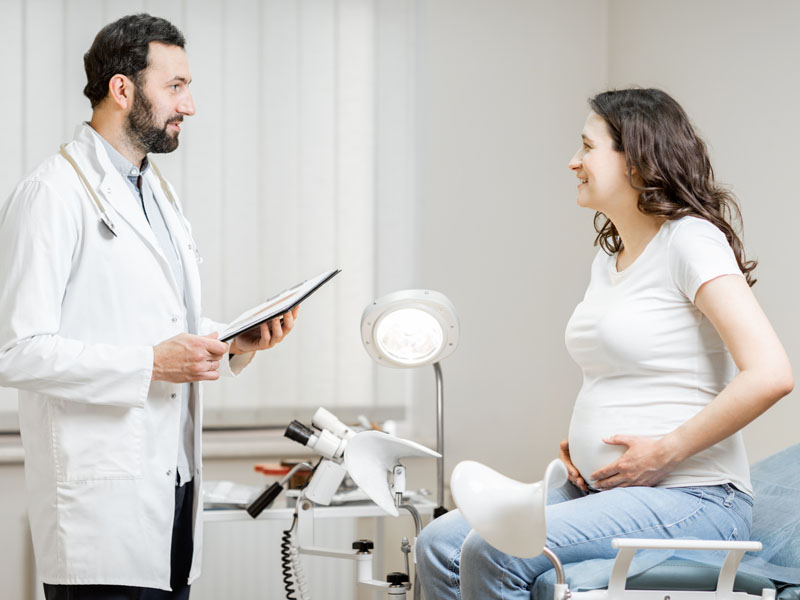 Doctor with clipboard talking to pregnant patient in exam room