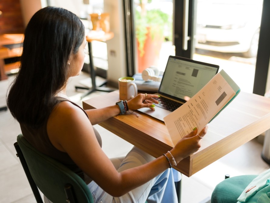 Woman at wooden desk working on computer while holding resume
